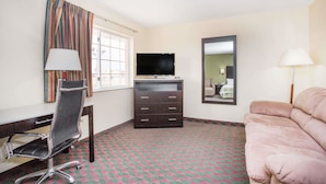 A hotel room with a desk, chair, TV, dresser, and a sofa.