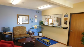 A reception area with a reception desk, a chair, a sofa, a small table, a computer, and a door.