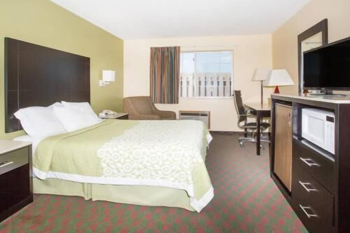 A hotel room with a bed, desk, chair, TV, and a window with curtains.