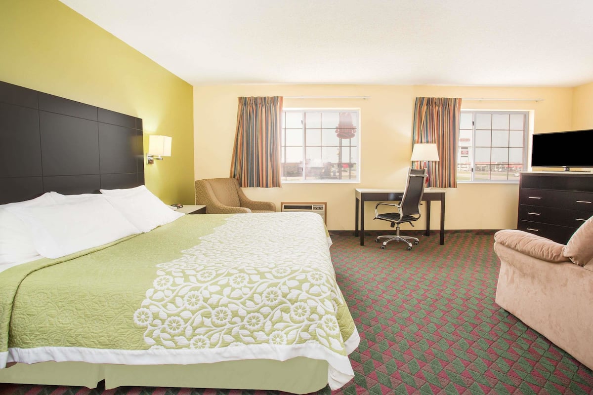 A hotel room with a large bed, a desk with a chair, a television, and two windows with curtains.