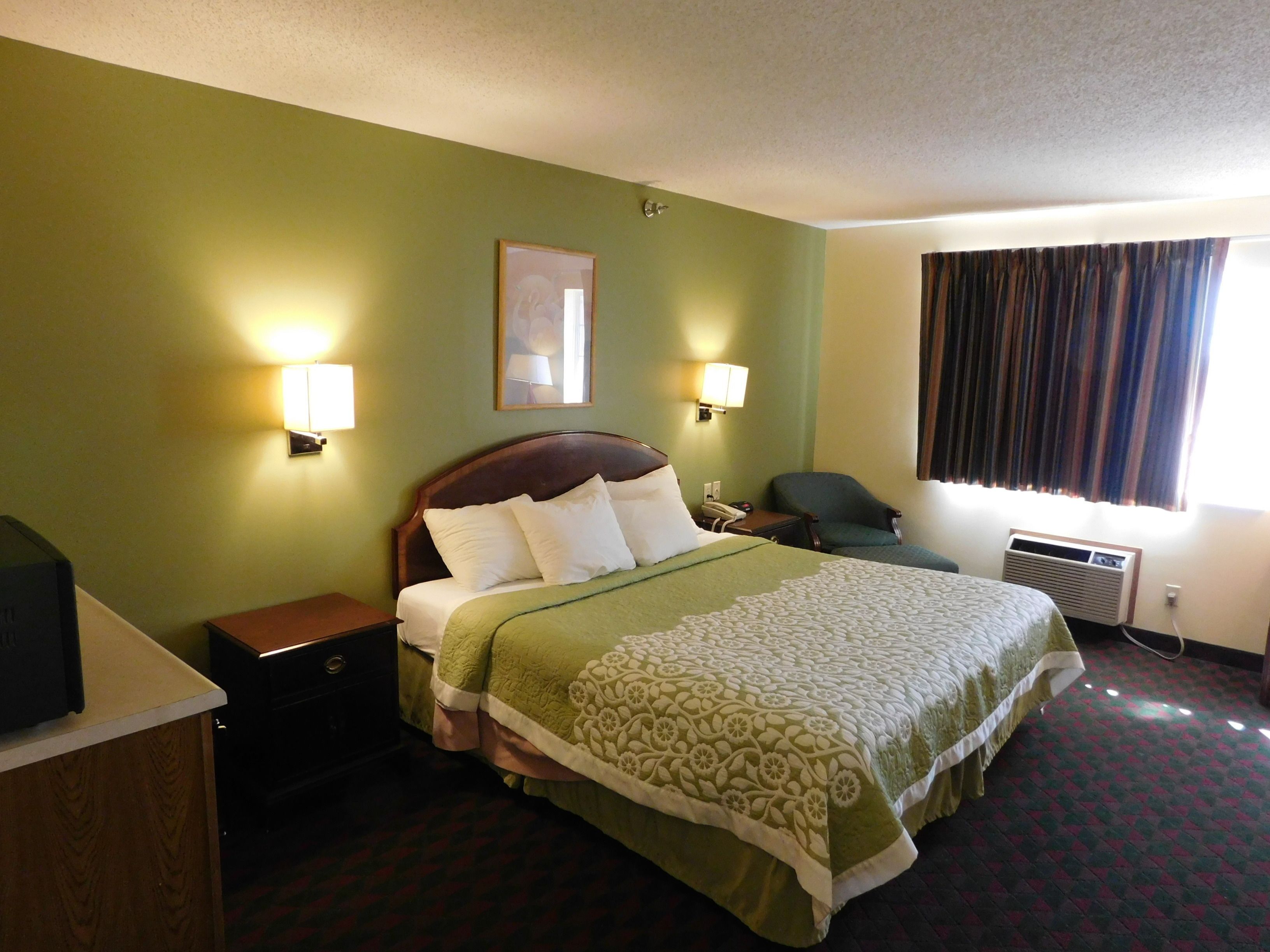 A hotel room with a large bed, two bedside lamps, a desk, and a window with curtains.