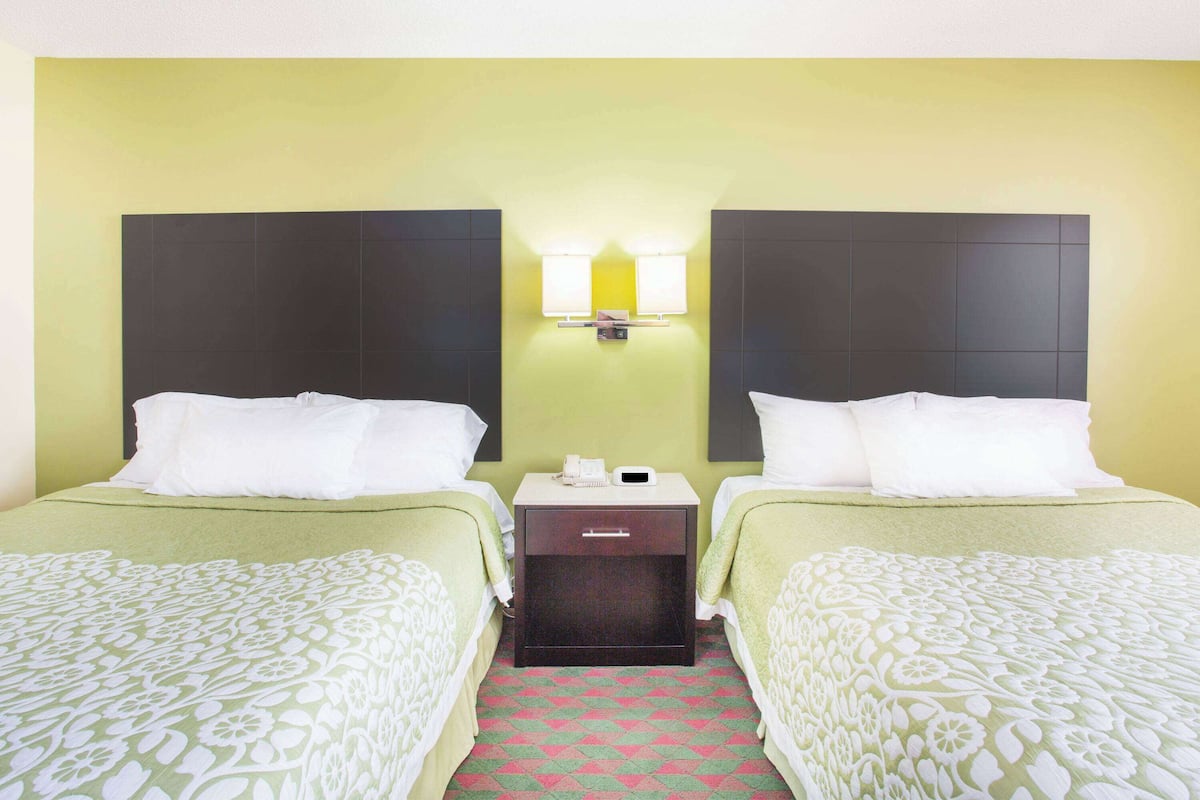 A hotel room with two beds, a nightstand, and a wall-mounted lamp.