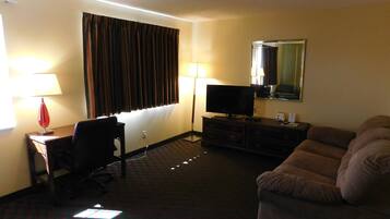 A hotel room with a desk, chair, television, sofa, and a mirror.