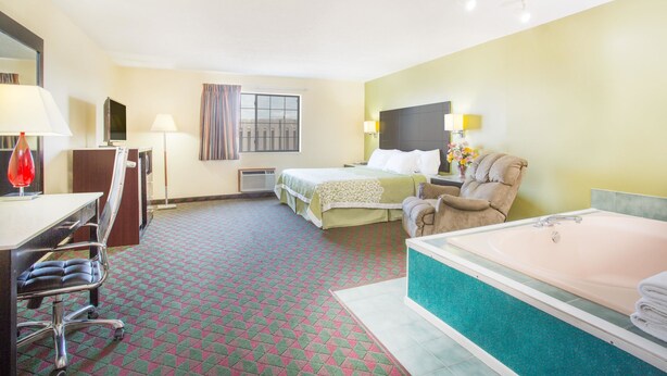 A hotel room with a bed, a desk with a chair, a bathroom with a bathtub, and a window with curtains.