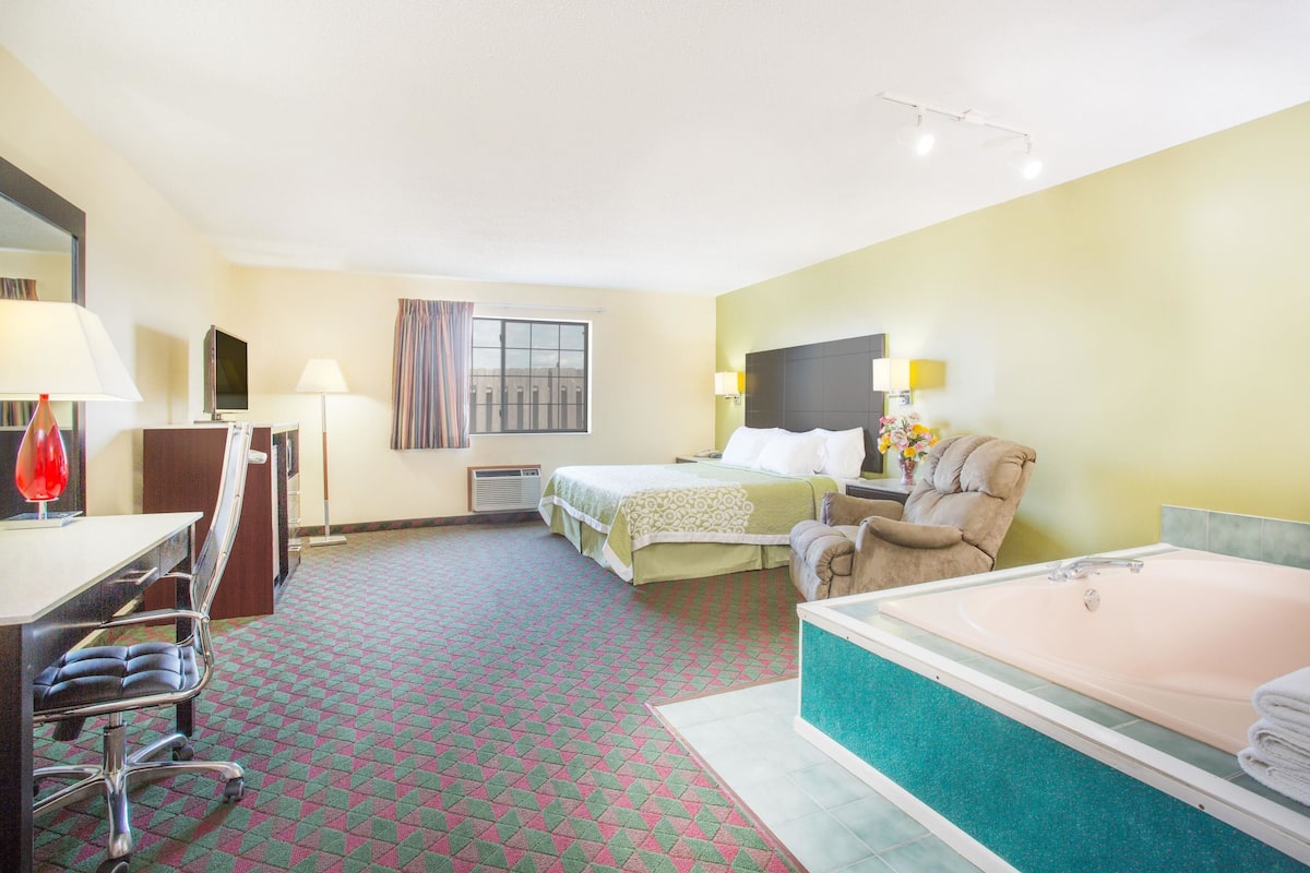 A hotel room with a bed, a desk with a chair, a bathroom with a bathtub, and a window with curtains.