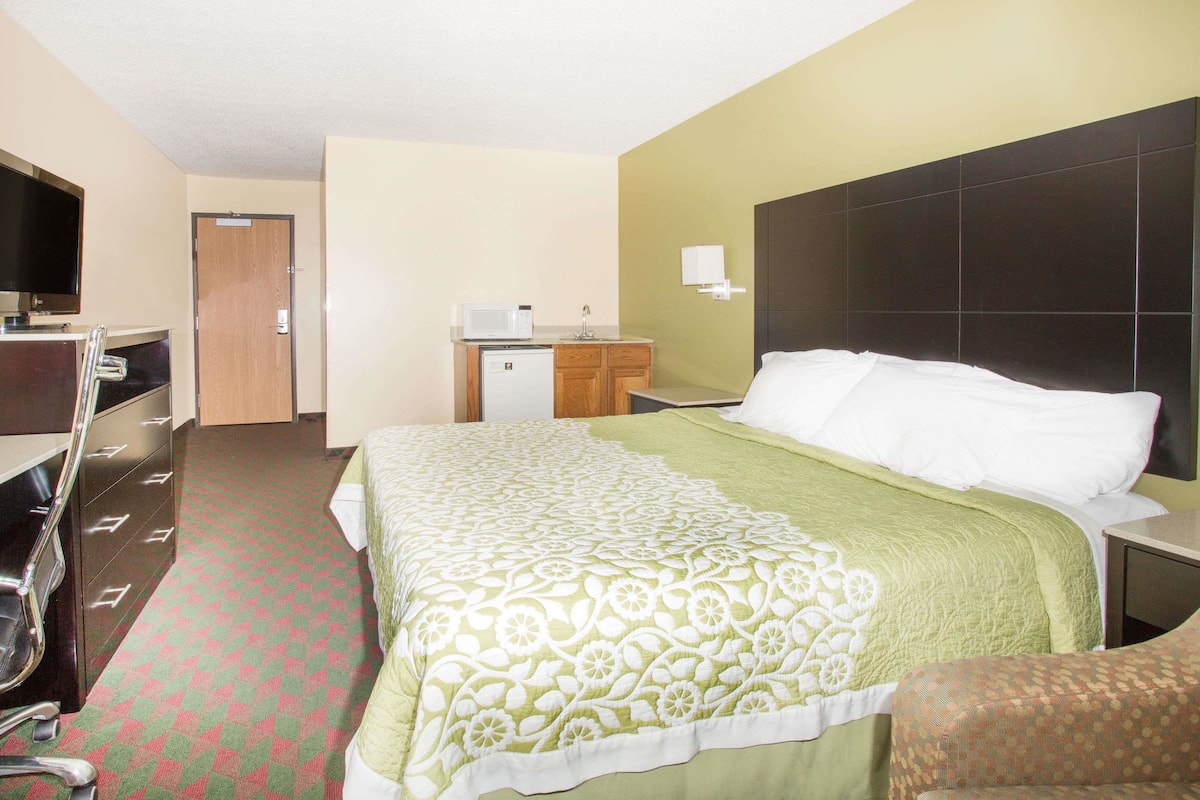 A hotel room with a bed, a desk, a chair, a microwave, and a small cabinet.