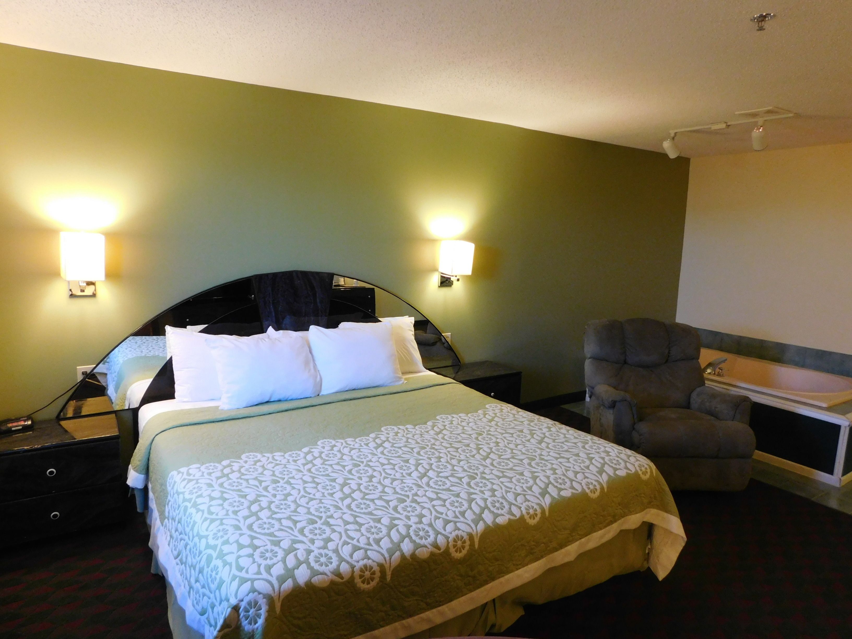 Habitación de hotel con cama, una silla, mesita de noche y lámpara de pared.