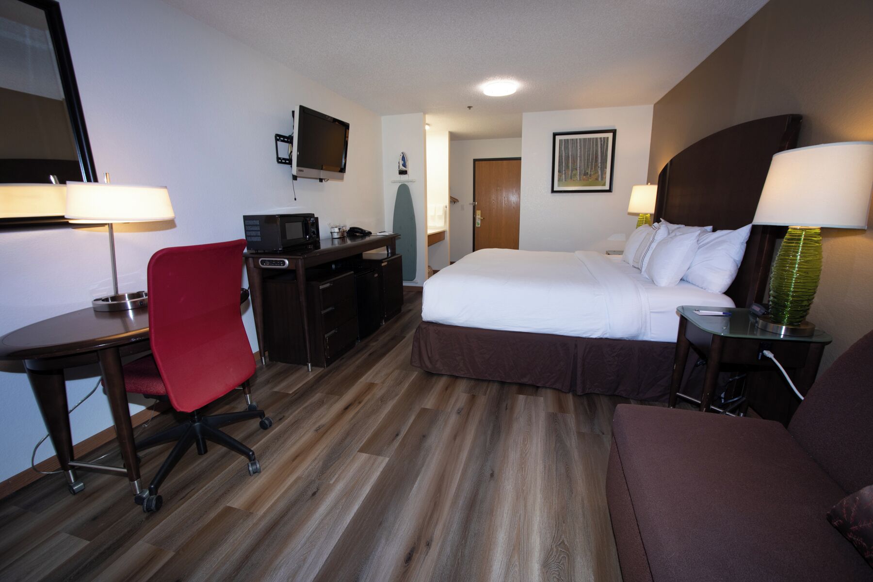 Habitación de hotel con cama, escritorio, silla, televisor y lámparas.