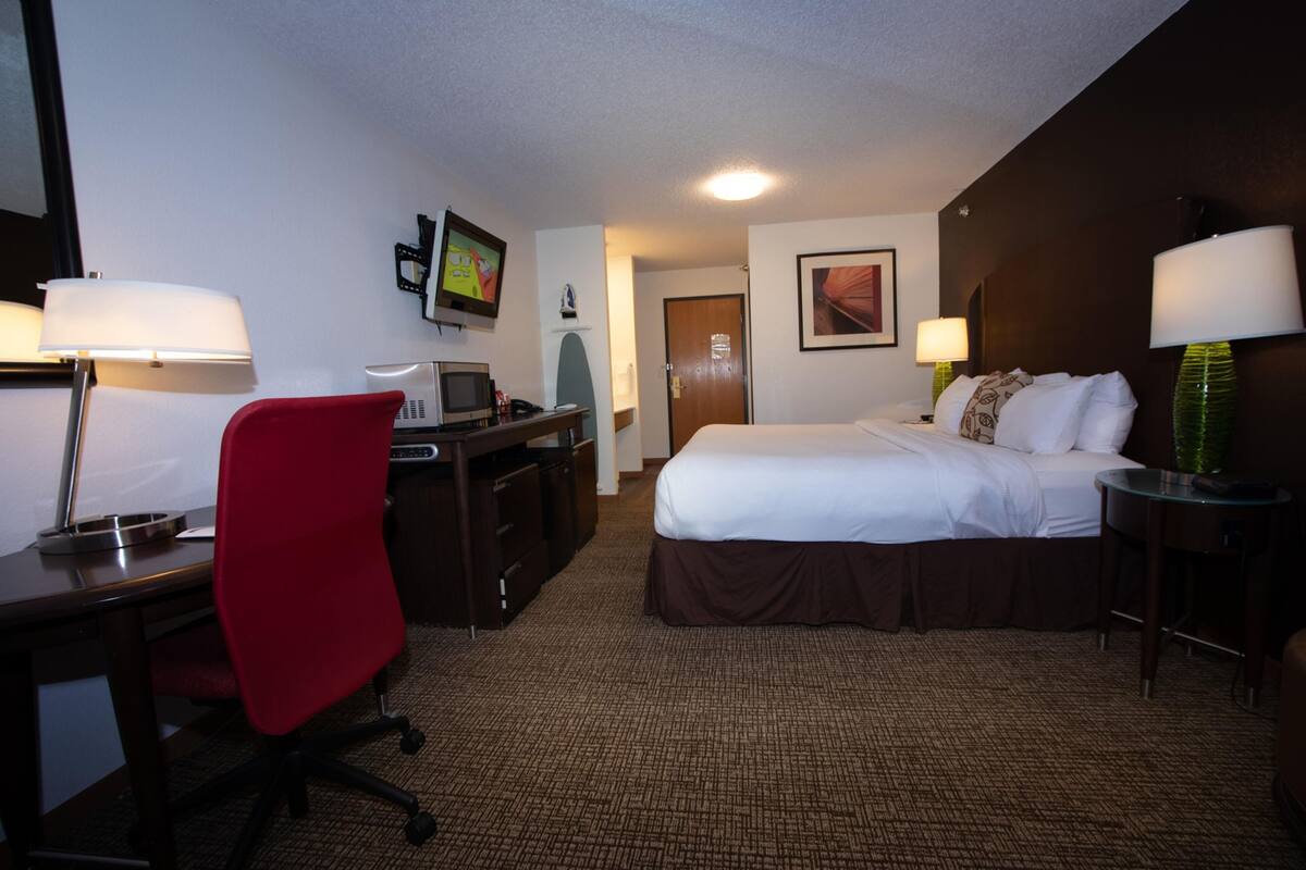 A hotel room with a bed, desk, chair, and a television on a stand.