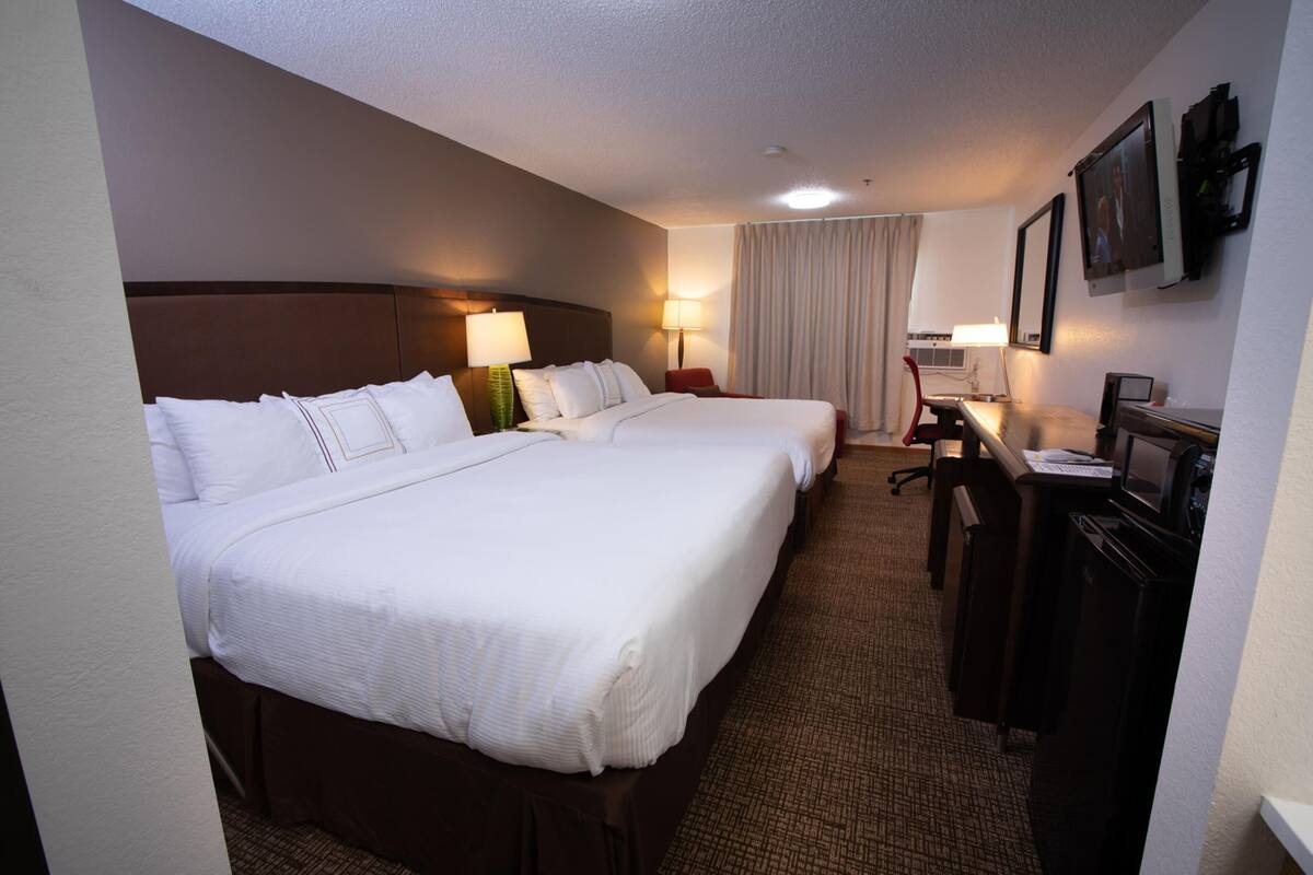 A hotel room with two beds, a desk, a chair, a TV, and a lamp.