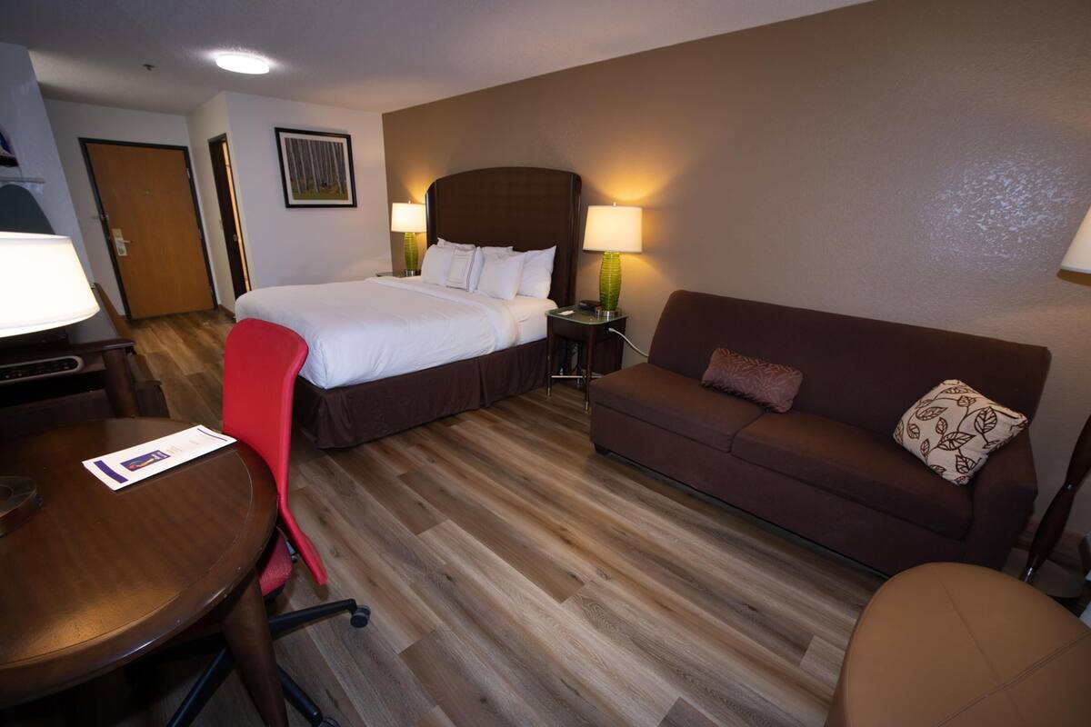 A hotel room with a bed, a sofa, a dining table, and a chair.