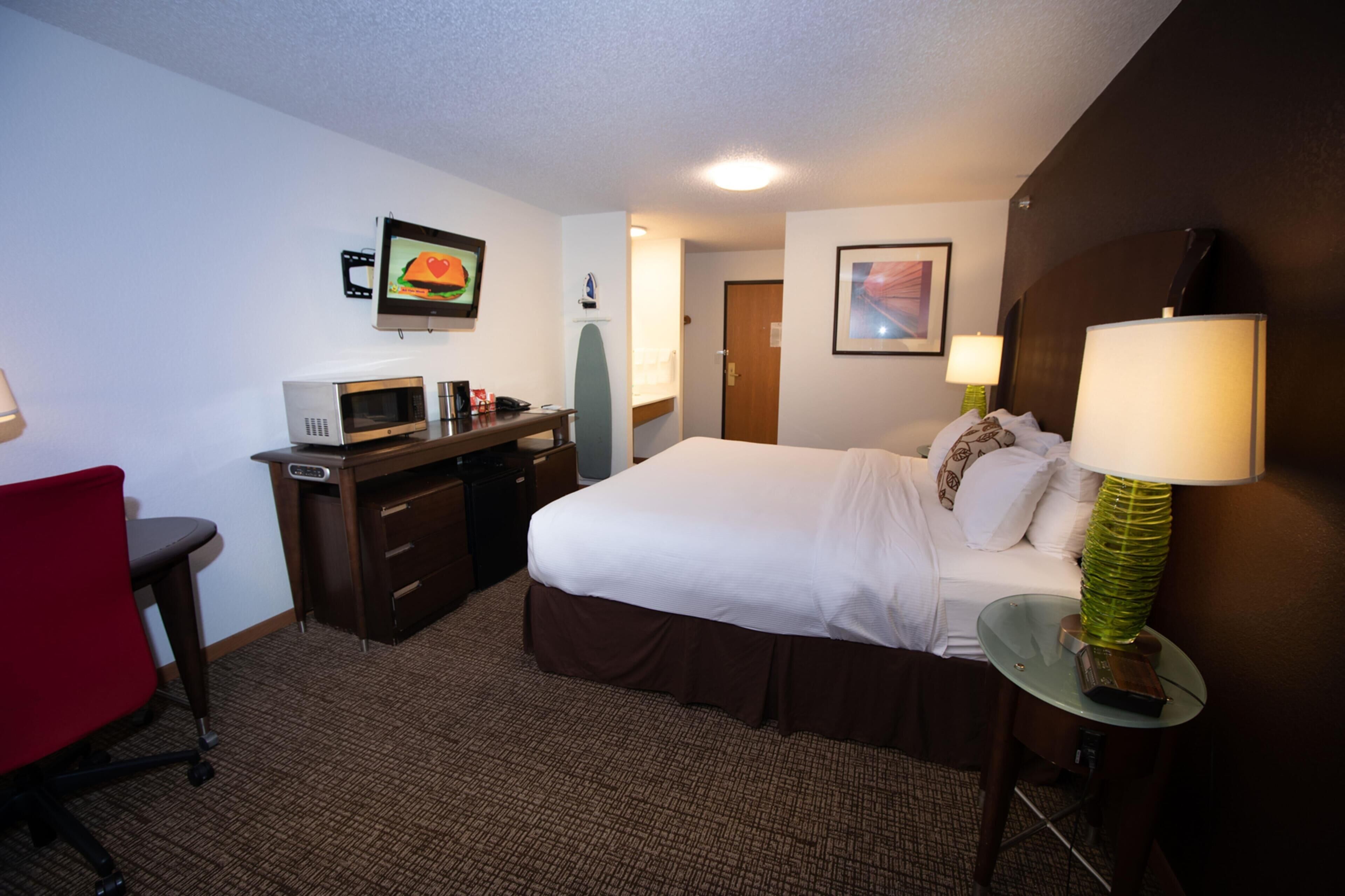 Habitación de hotel con cama, escritorio, silla, microondas y televisión en la pared.