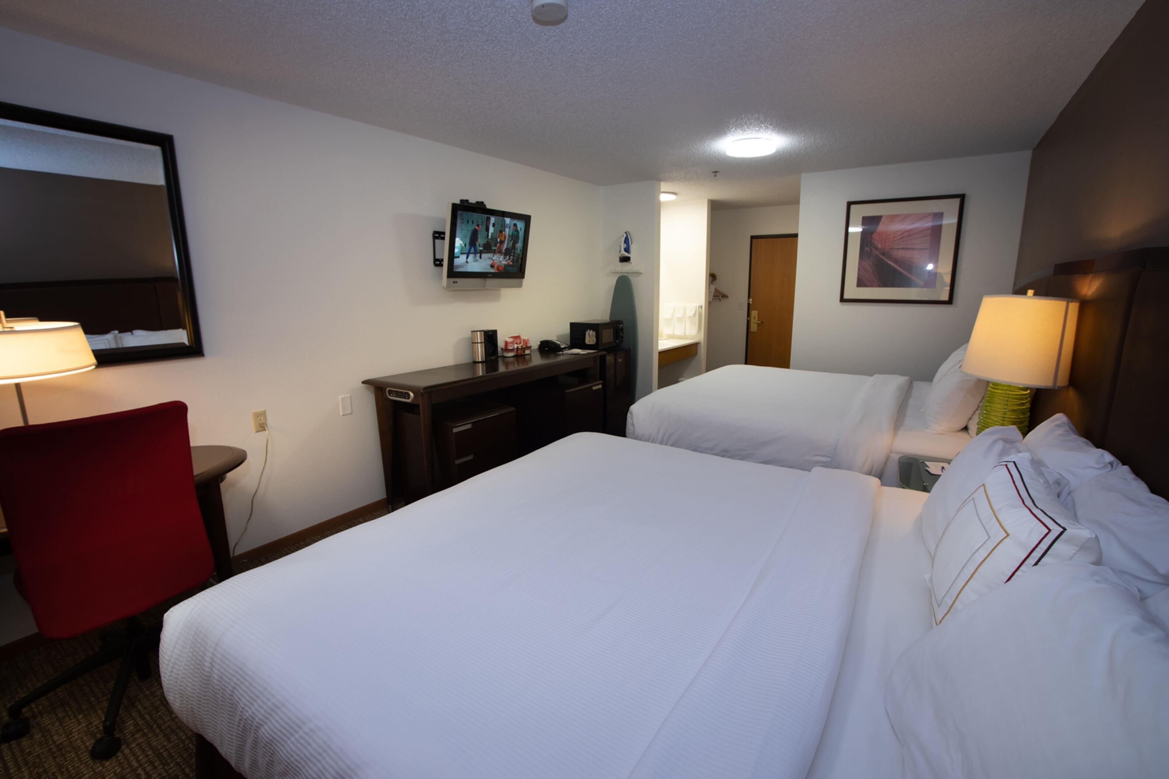 A hotel room with two beds, a desk with a chair, a TV, and a mirror.