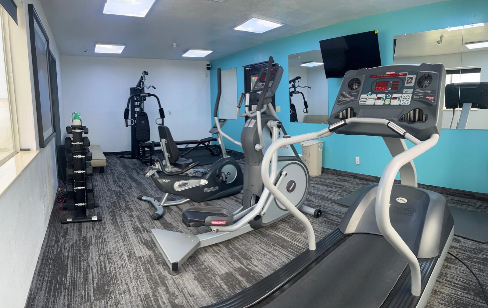 A gym with cardio machines, weight benches, and a mirrored wall.