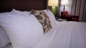 A neatly made bed with white bedding and a decorative pillow with a leaf pattern.