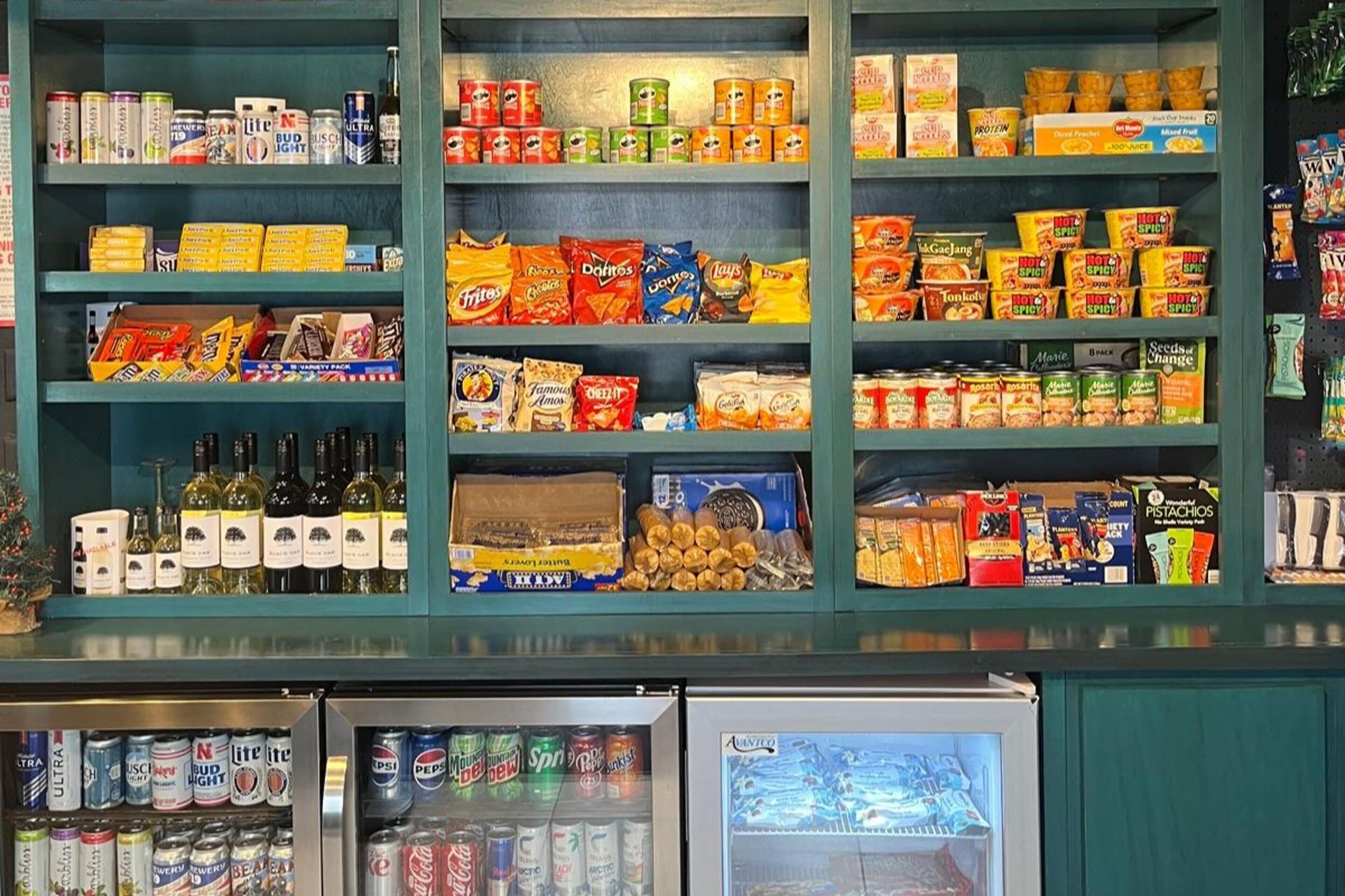 Un présentoir proposant une variété de collations et de boissons de différentes marques et de différents types, notamment des chips et des noix, ainsi qu’un assortiment de bières et de sodas.