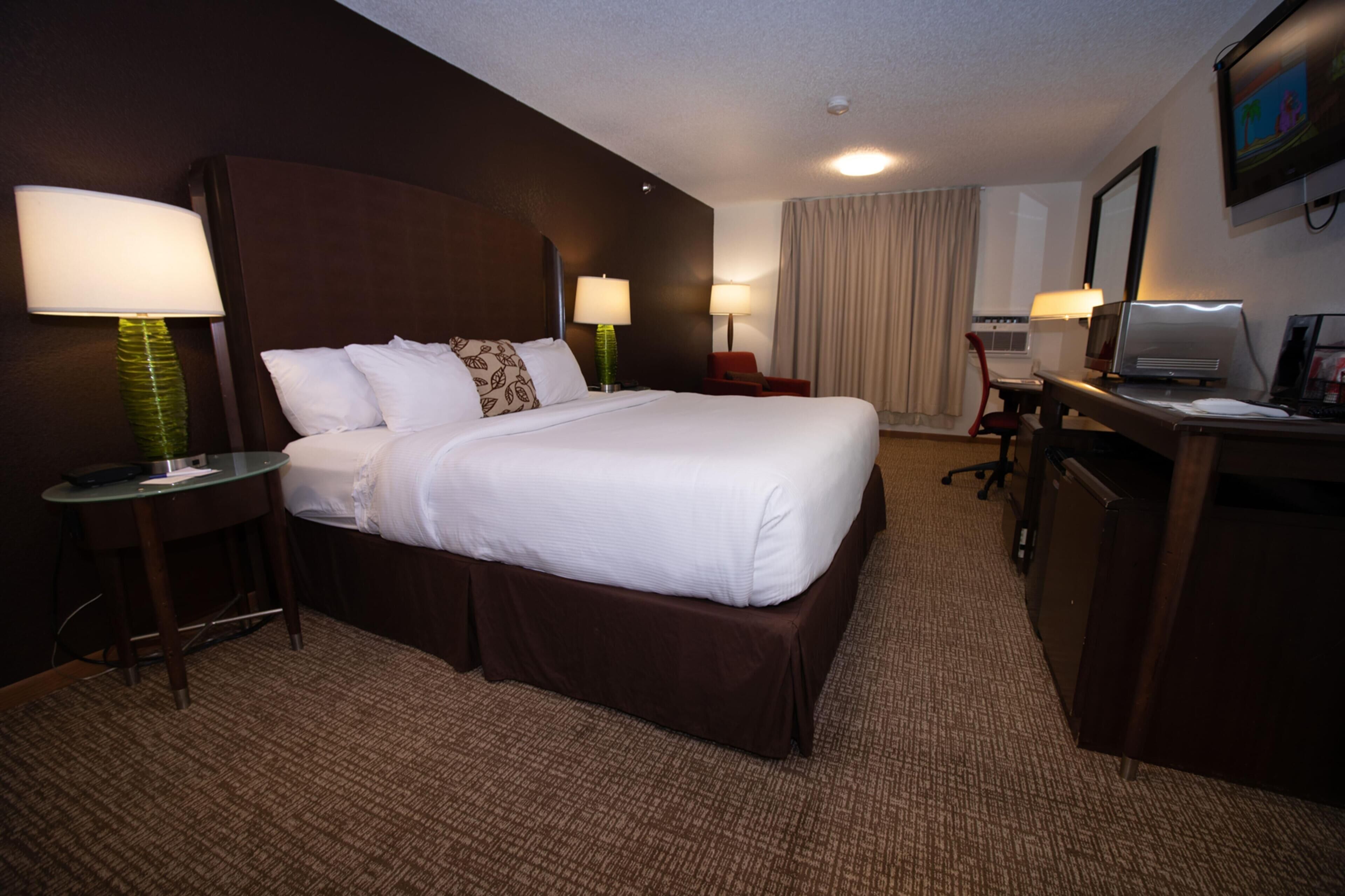 Une chambre d’hôtel avec un grand lit, deux tables de chevet avec des lampes, un bureau avec un ordinateur et un téléviseur fixé au mur.