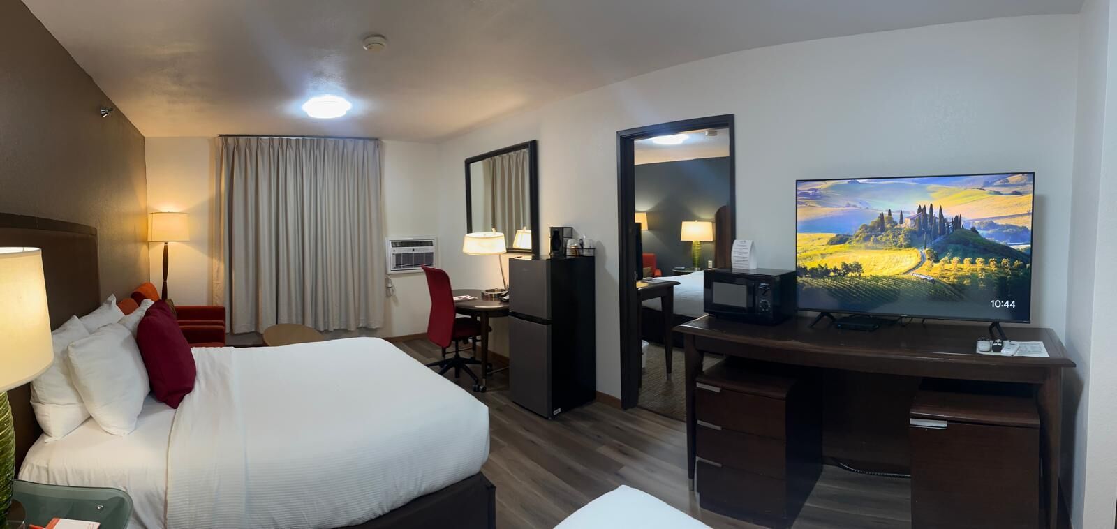 Una habitación de hotel con cama, escritorio, silla, televisor y un ventanal con cortinas.