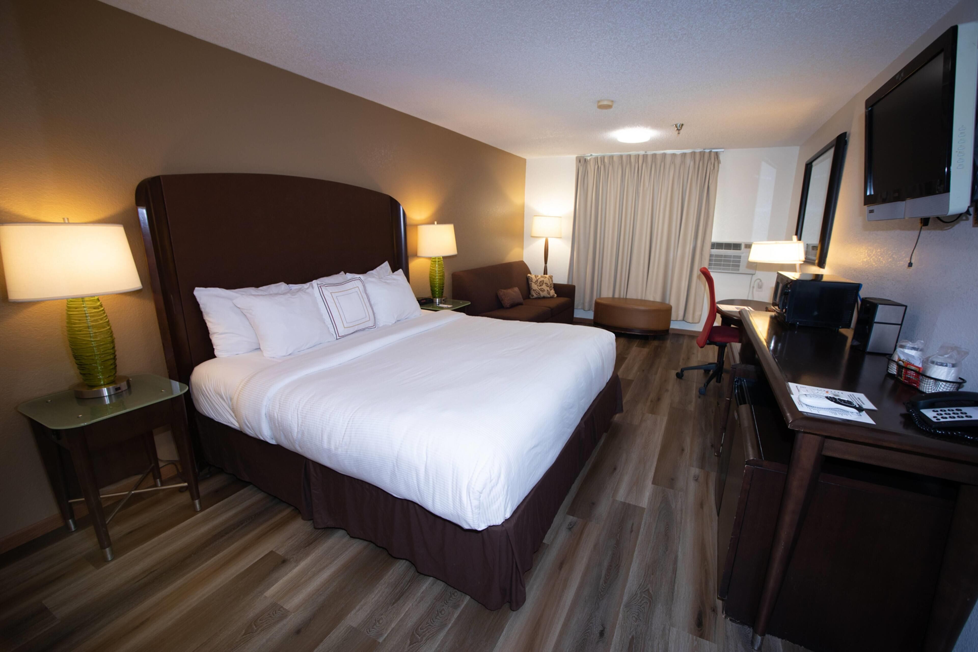 A hotel room with a large bed, two bedside tables with lamps, a desk with a computer, a chair, and a TV mounted on the wall.