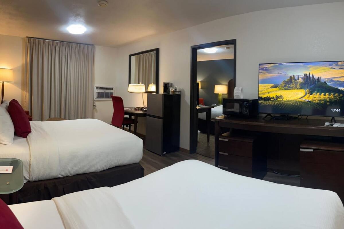 A hotel room with two beds, a desk, a television, a mirror, a lamp, and a window with curtains.