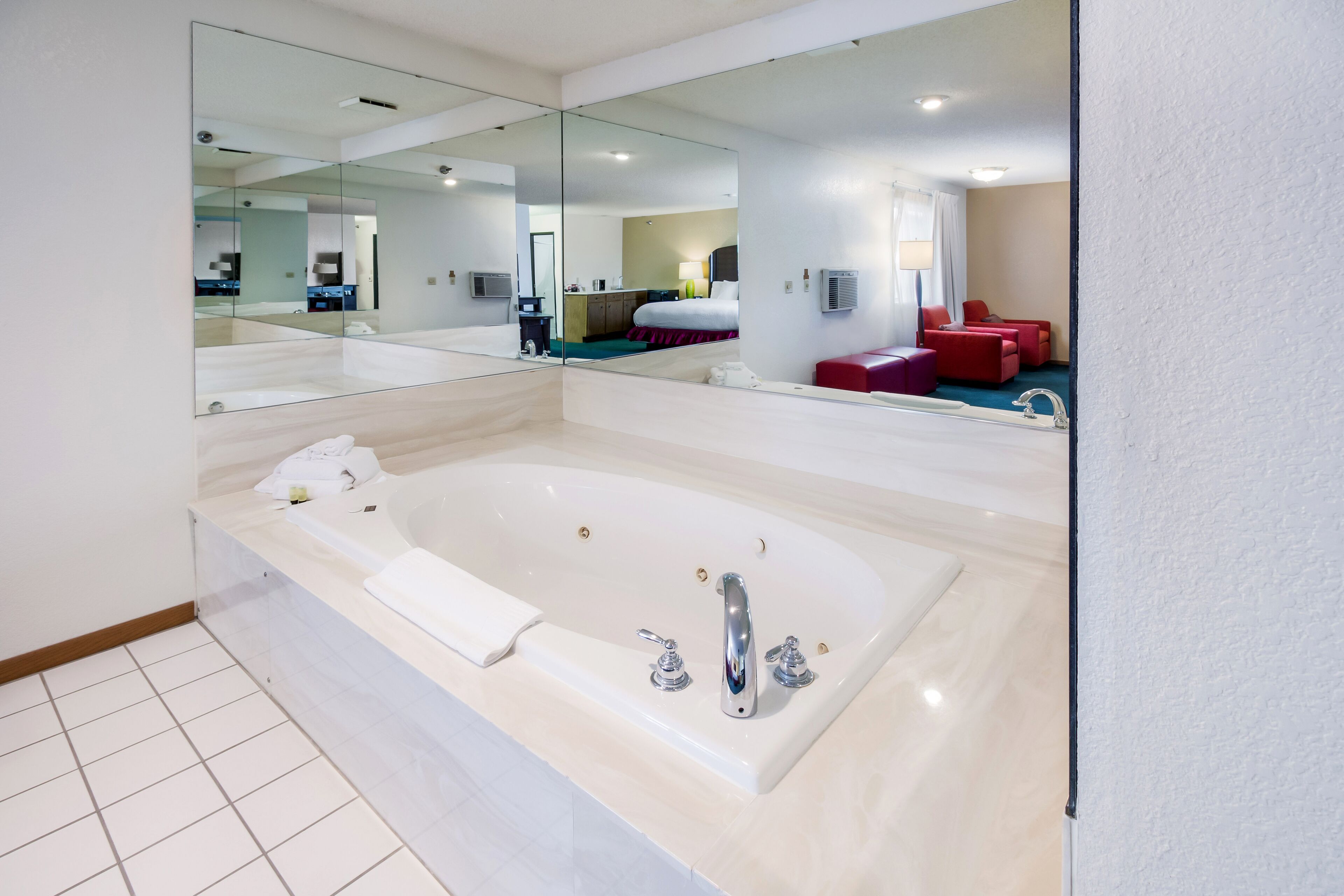 A modern bathroom with a large bathtub, a mirror, and a red seating area.