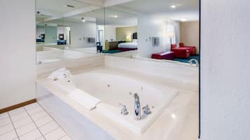 A modern bathroom with a large bathtub, a mirror, and a red seating area.