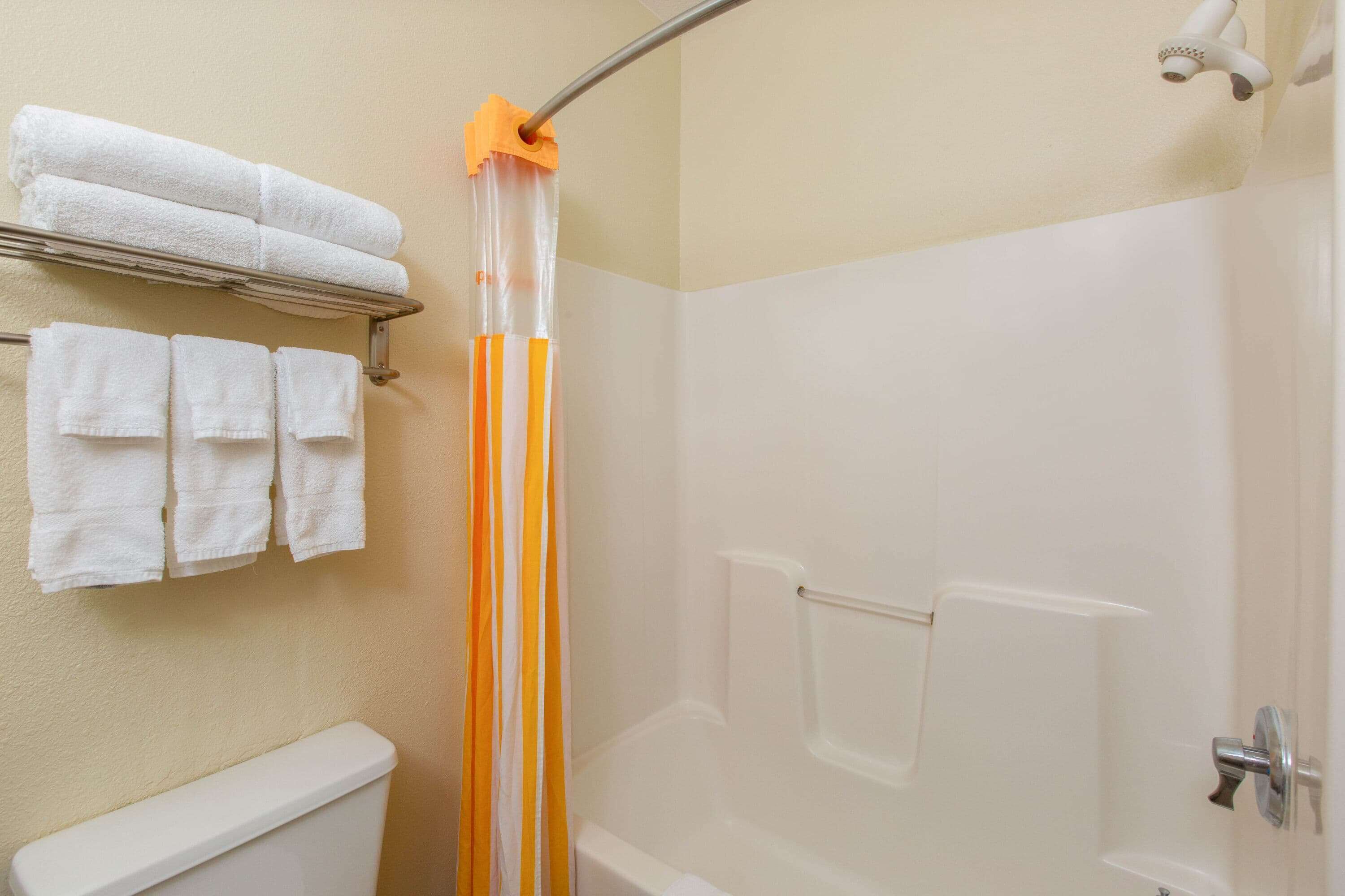 A bathroom with a shower, a toilet, and a towel rack with folded towels.