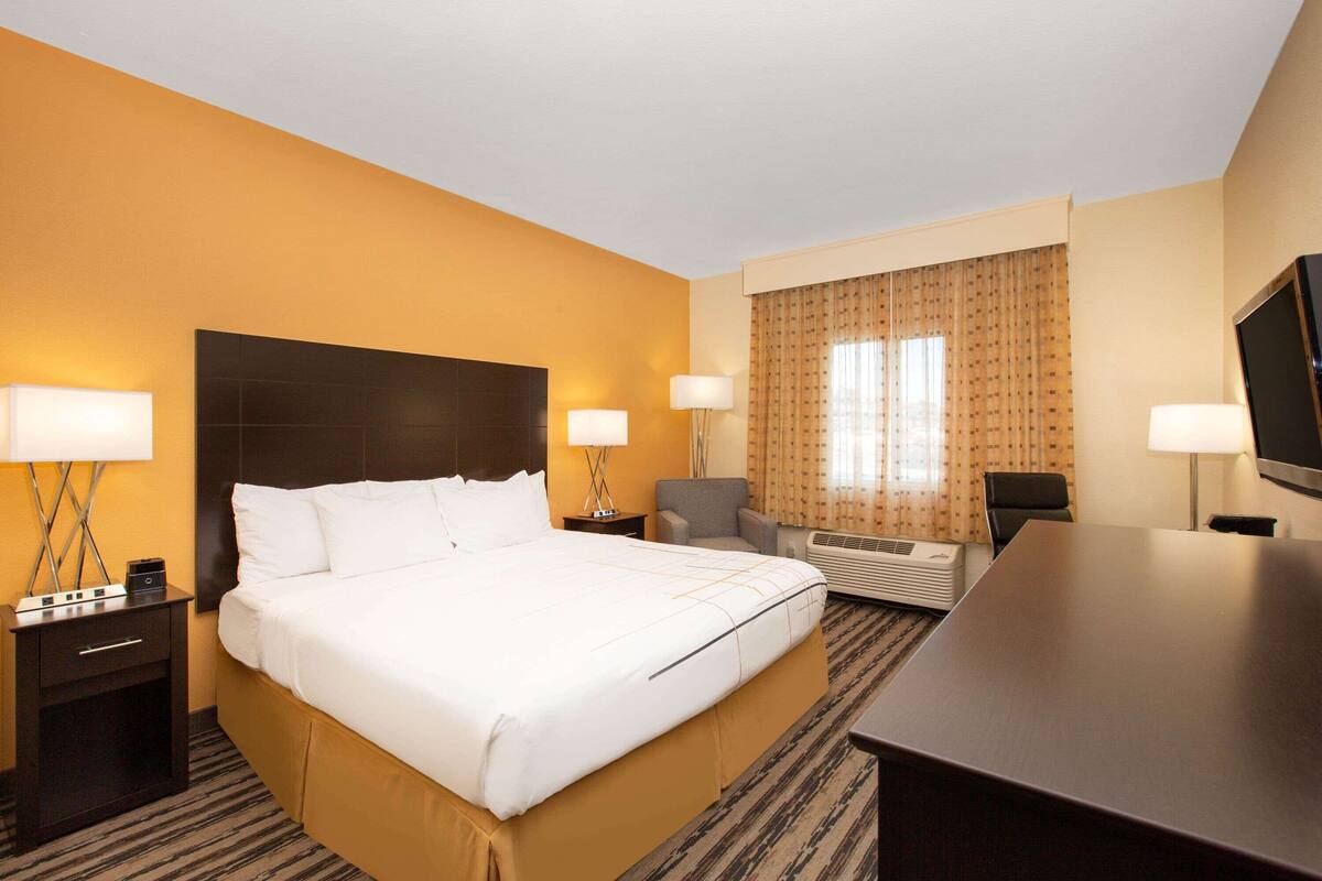 A hotel room with a large bed, two bedside tables with lamps, a desk, a chair, and a television.