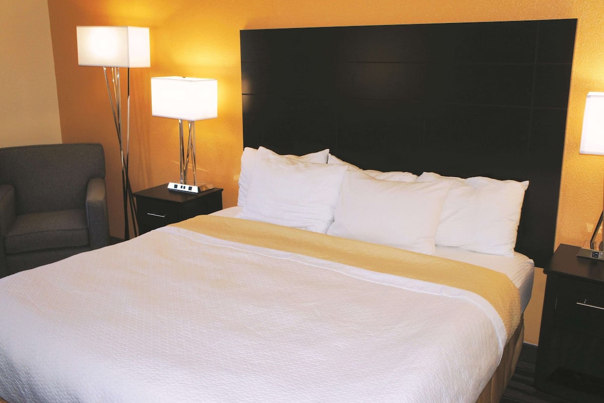 A hotel room with a large bed, two bedside tables, a chair, and two floor lamps.