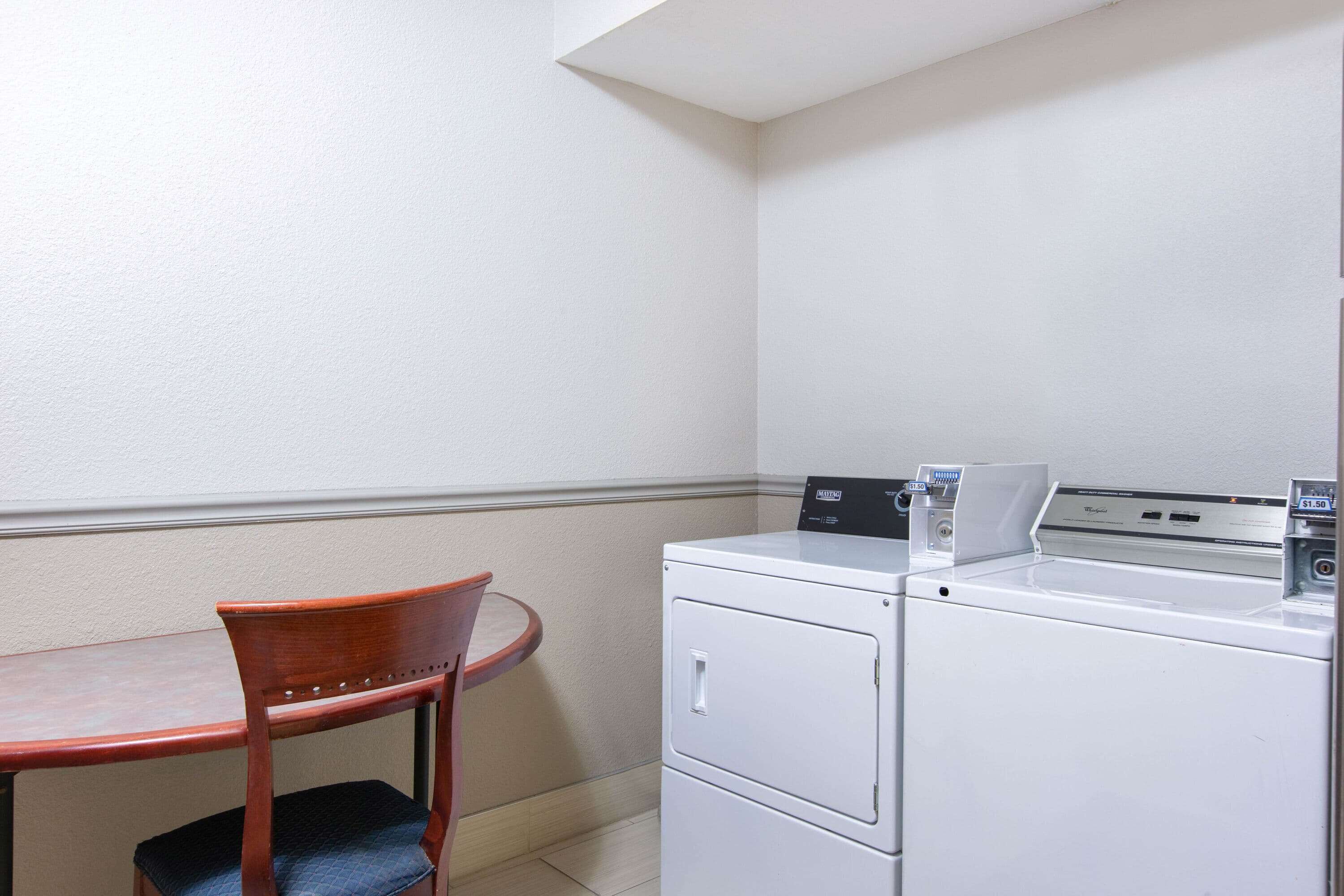 A small room with a table and a chair, a washing machine, and a wall-mounted heater.