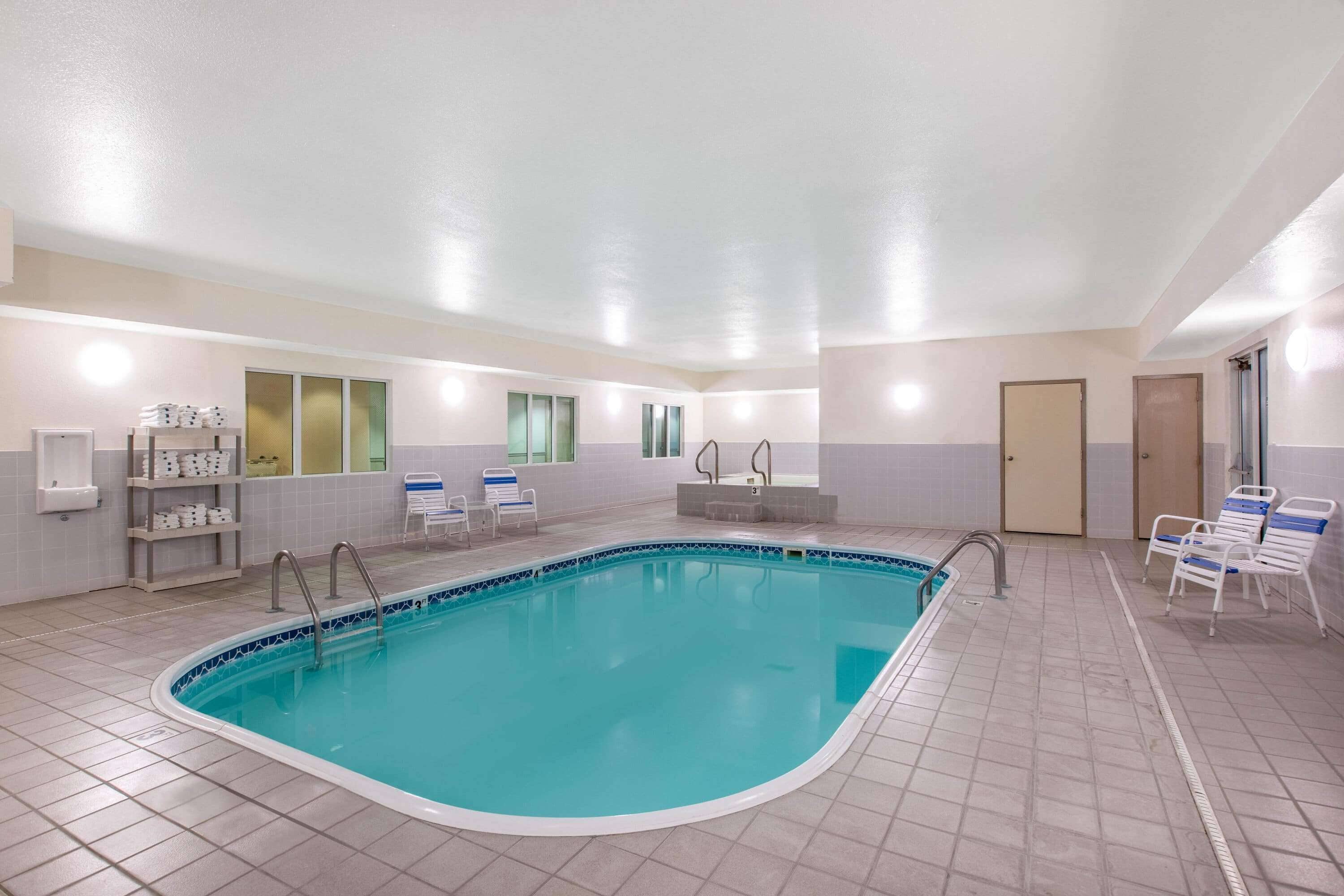 Una piscina con suelo y paredes de azulejos, una escalera de piscina y varias sillas de descanso.
