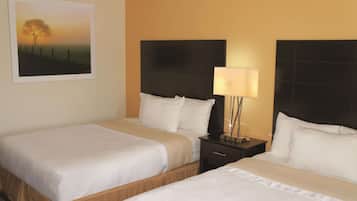 Habitación de hotel con dos camas, una mesita de noche con lámpara y un cuadro enmarcado en la pared.