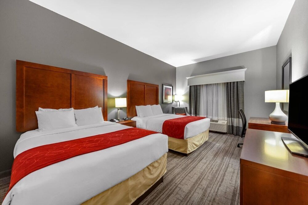 A hotel room with two beds, a desk, a TV, and a window with curtains.
