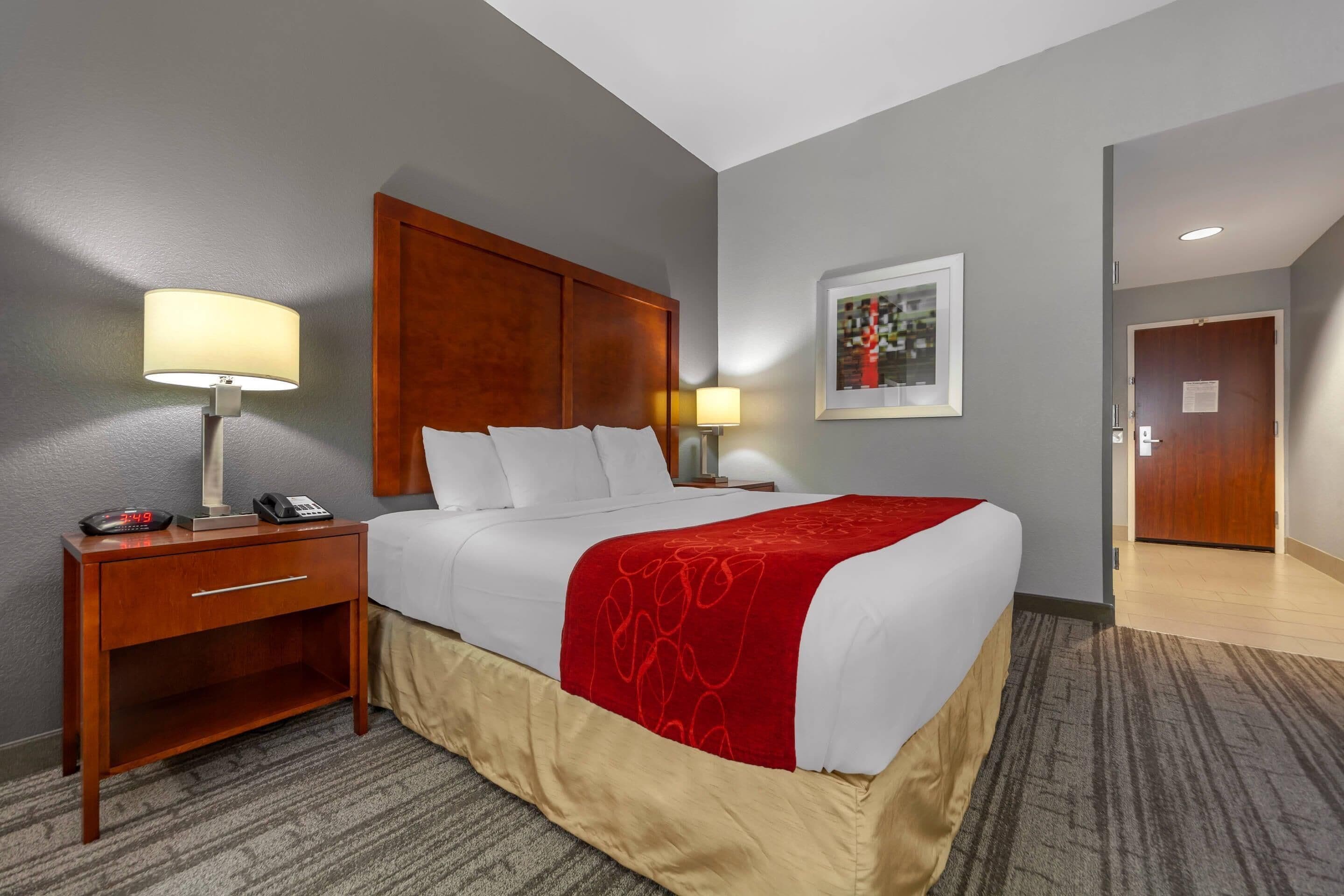 A hotel room with a bed, bedside table, lamp, and a painting on the wall.