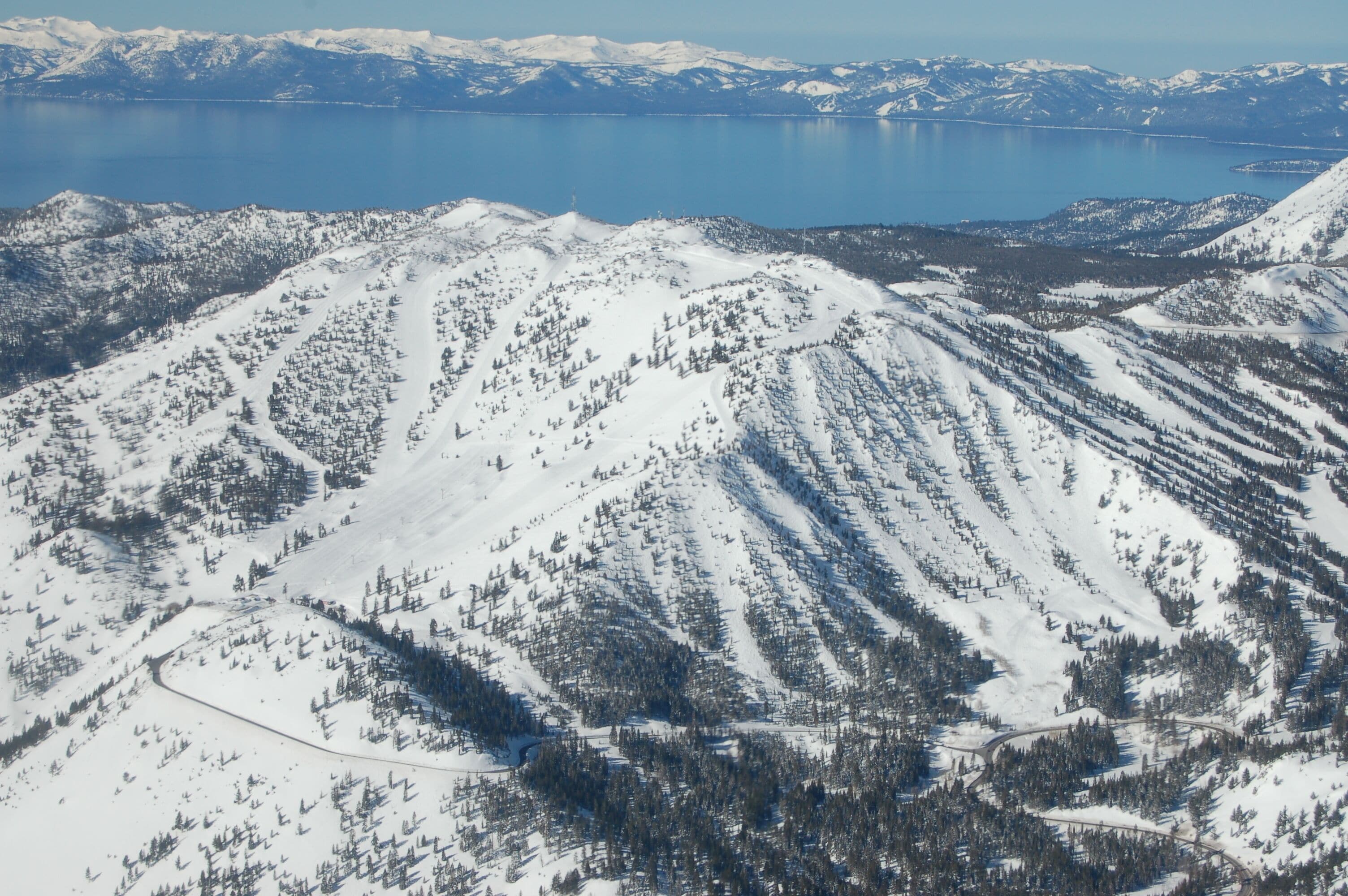 A snow-covered mountain with a clear view of a lake and distant mountains.