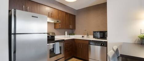 A modern kitchen with stainless steel appliances, wooden cabinets, and a built-in microwave.