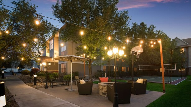 Un patio al aire libre con luces colgantes, mobiliario exterior y una cancha de baloncesto.