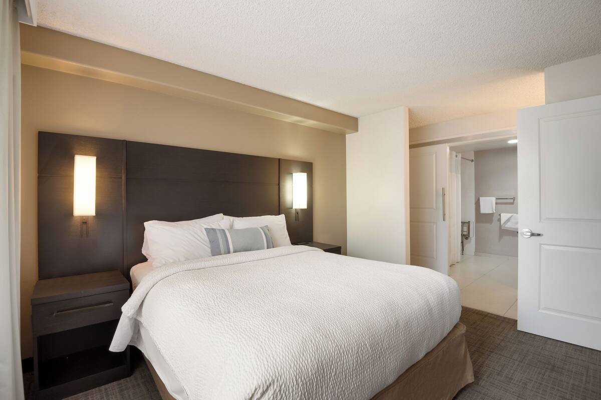 A hotel room with a large bed, bedside tables, a nightstand, and a wall-mounted light fixture.