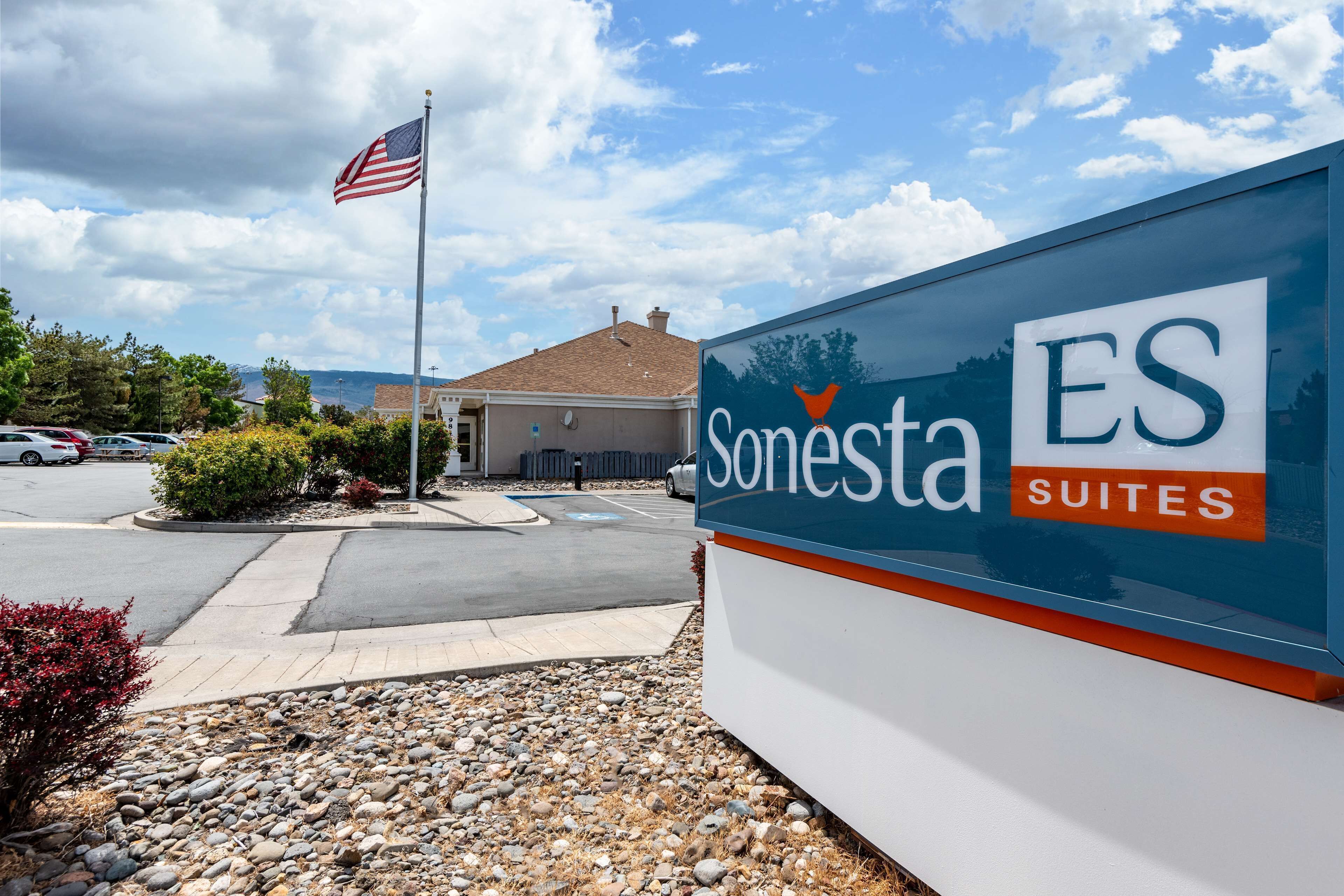 A sign for Sonesta Suites with a clear view of the surrounding area, including a parking lot and a building in the background.
