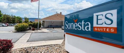 A sign for Sonesta Suites with a clear view of the surrounding area, including a parking lot and a building in the background.