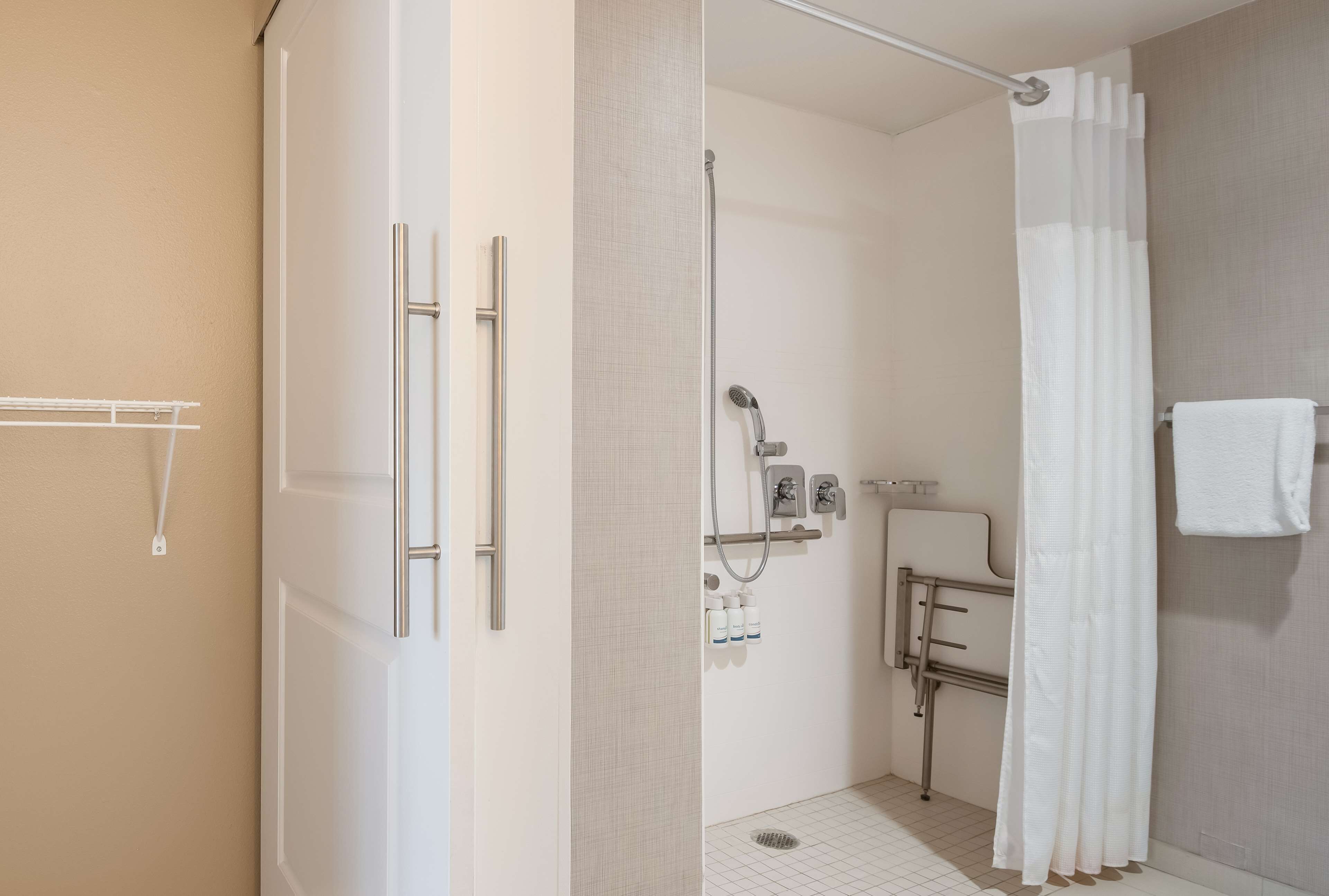 A modern bathroom with a walk-in shower, a toilet with grab bars, and a towel rack.
