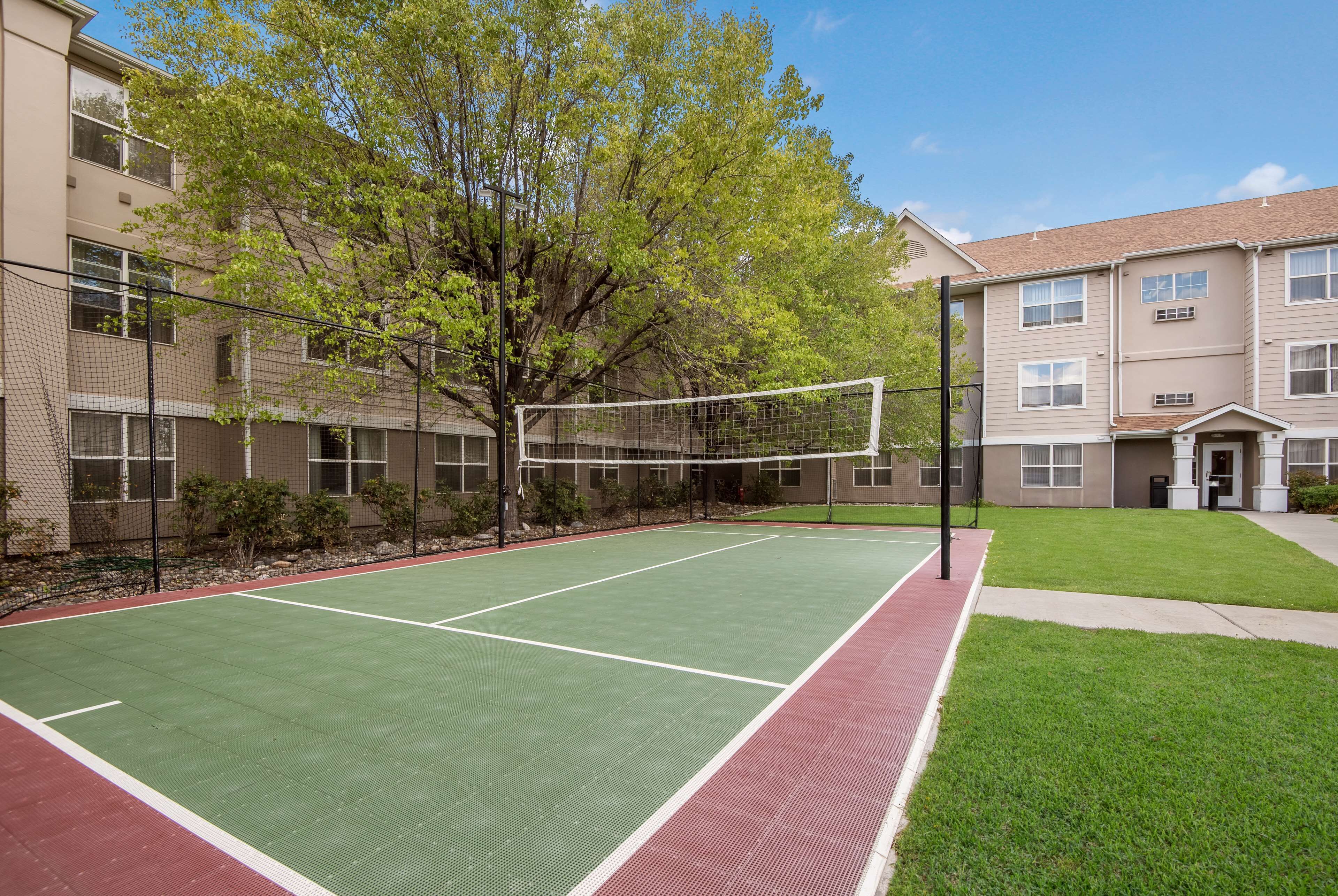 An outdoor tennis court with a net, surrounded by a fence and trees.