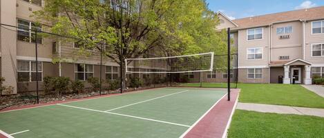 An outdoor tennis court with a net, surrounded by a fence and trees.