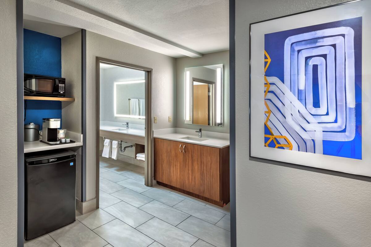 A modern bathroom with a wooden vanity, a large mirror, and a microwave on a shelf.