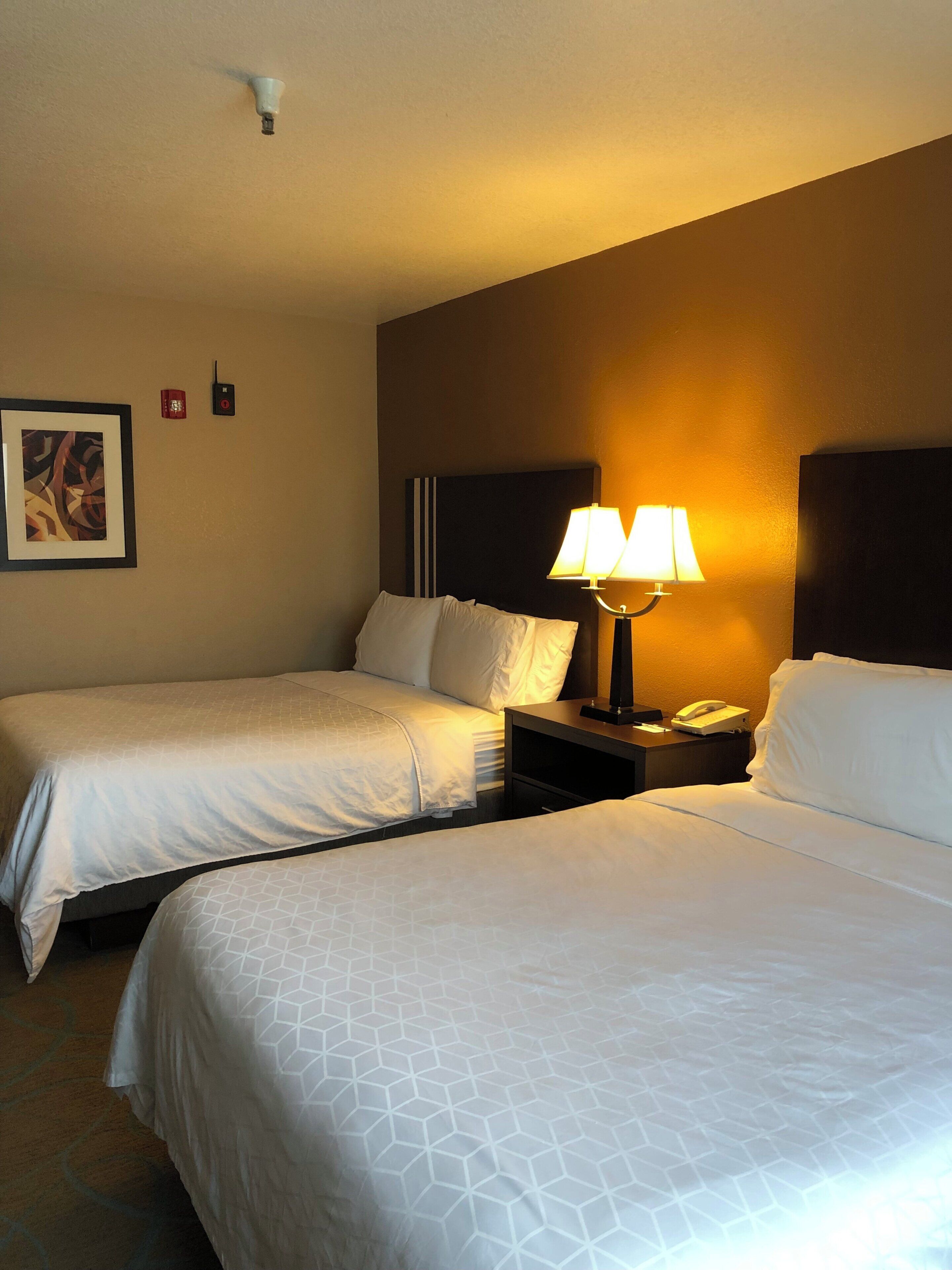 Une chambre d’hôtel avec deux lits, une table de chevet avec une lampe, un téléphone et un tableau au mur.