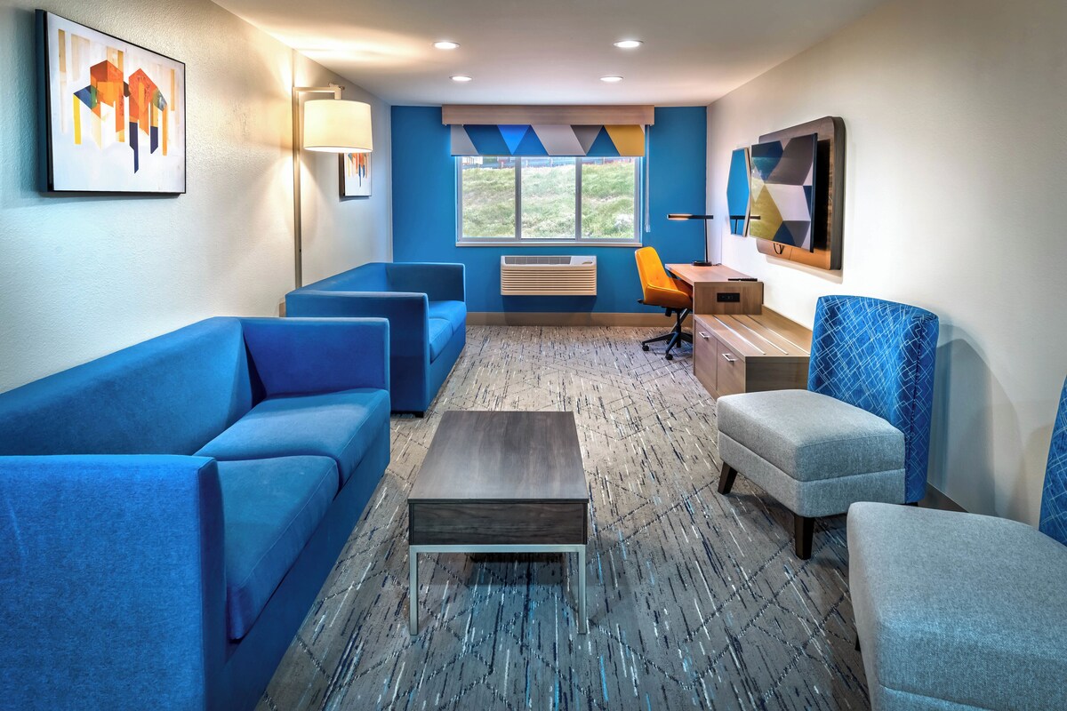 Une pièce moderne avec des canapés bleus, une table basse, un bureau avec une chaise et une grande fenêtre.