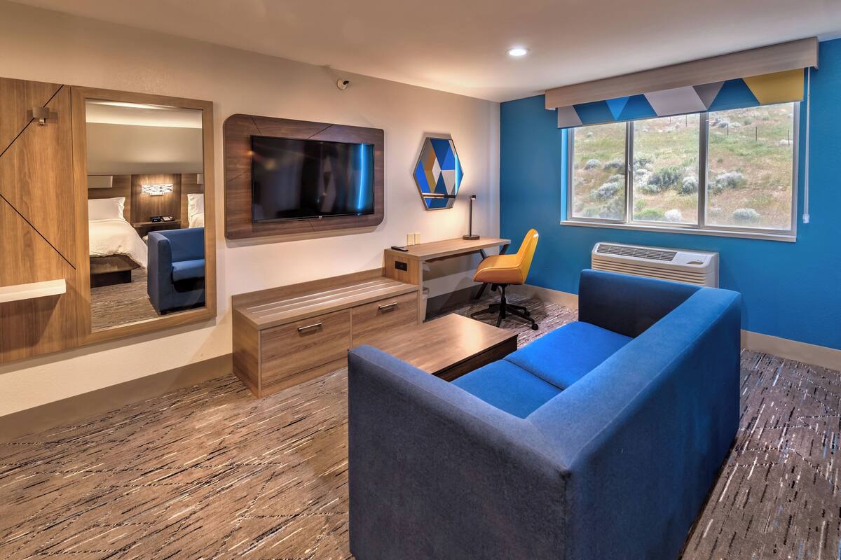 A modern room with a large bed, a TV, a desk, and a blue sofa.