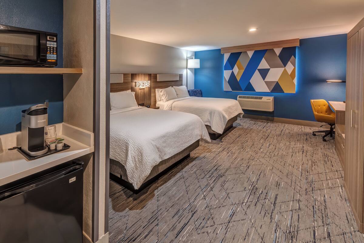 A hotel room with two beds, a microwave, a coffee maker, a desk, and a chair.