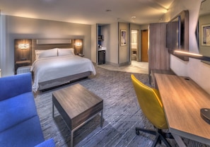 A modern hotel room with a large bed, a desk, a chair, and a TV mounted on the wall.