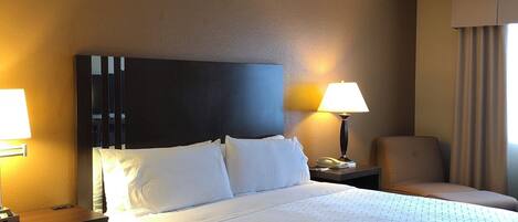 Una habitación de hotel con una cama grande, dos mesitas de noche, una silla, un escritorio y una lámpara.